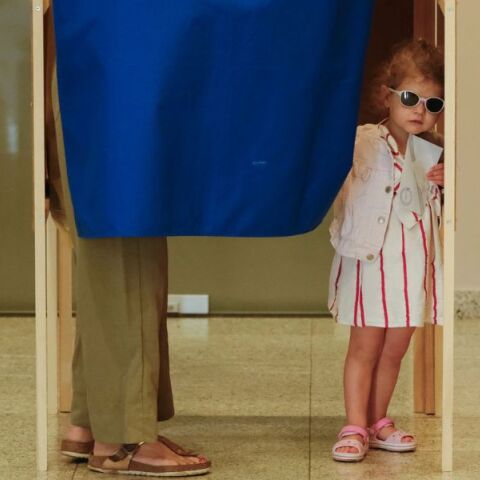 Ένα κοριτσάκι φαίνεται στην άκρη του παραβάν την ώρα που η μητέρα της ψηφίζει