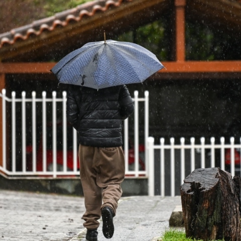 ανδρας περπαταει στη βροχη με ομπρελα