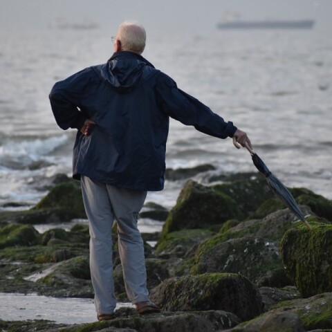 Ηλικιωμένος με ομπρέλα στην ακτή με φόντο τη θάλασσα