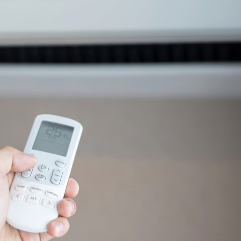 Χέρι με το κοντρόλ του κλιματιστικού μπροστά από το κλιματιστικό