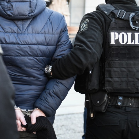 Άτομο που φορά χειροπέδες και κρατείται από αστυνομικούς