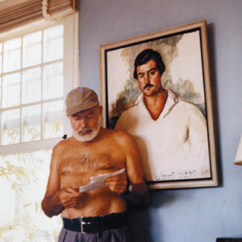 Ο Έρνεστ Χέμινγουεϊ στο σπίτι του στην Κούβα, μπροστά από το πορτρέτο του, περίπου το 1953