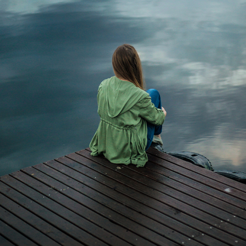 woman sitting on dock near body of water