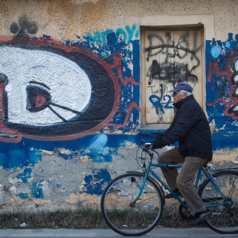 Ηλικιωμένος ποδηλάτης περνά μπροστά από γκράφιτι σε τοίχο εγκαταλειμμένου σπιτιού 