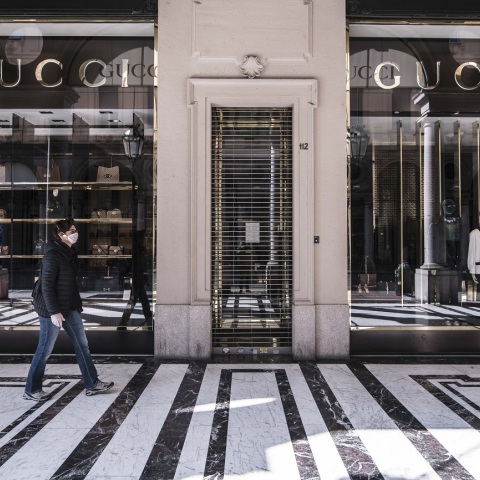 Γυναίκα με μάσκα περπατάει έξω από ένα κλειστό κατάστημα Gucci