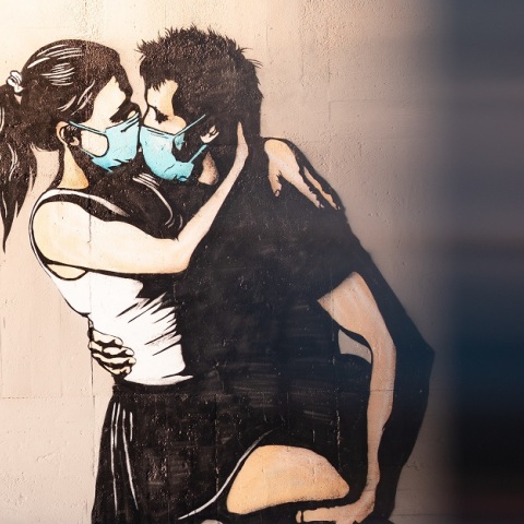 Γκράφιτι με ζευγάρι που φιλιέται φορώντας χειρουργικές μάσκες