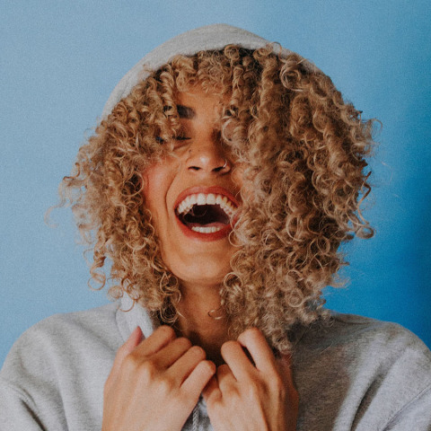 Κοπέλα με σγουρά μαλλιά φοράει κουκούλα και γελάει