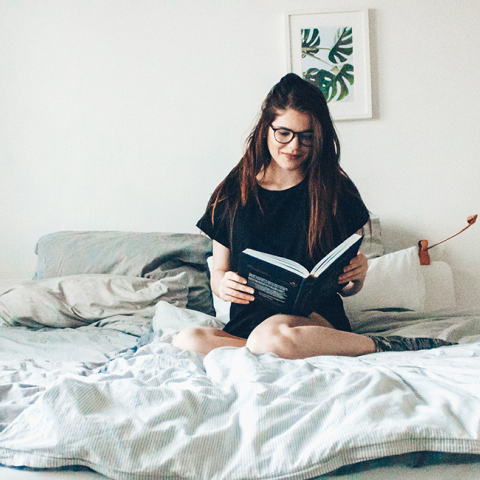 Κοπέλα που κάθεται στο κρεβάτι και διαβάζει βιβλίο