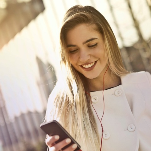 Μία κοπέλα κρατάει ένα κινητό και φοράει ακουστικά