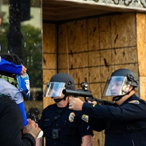 Αστυνομικός σημαδεύει με το όπλο του Αφροαμερικανό που κρατά στους ώμους ένα μικρό κοριτσάκι