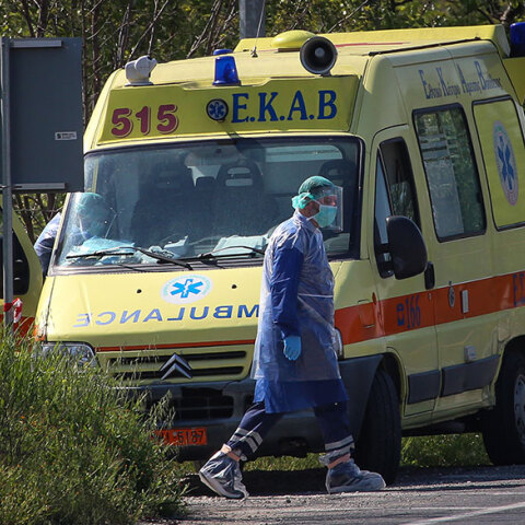 Τραυματιοφορέας με προστατευτική στολή για κορωνοϊό περνά μπροστά από ασθενοφόρο του ΕΚΑΒ