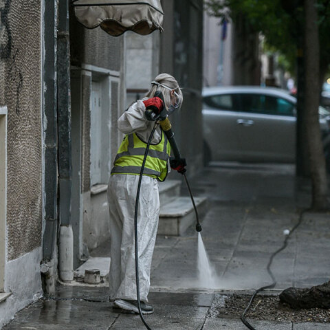 Υπάλληλος του Δήμου Αθηναίων με προστατευτική στολή για τον κορωνοϊό απολυμαίνει πεζοδρόμιο στο κέντρο της Αθήνας