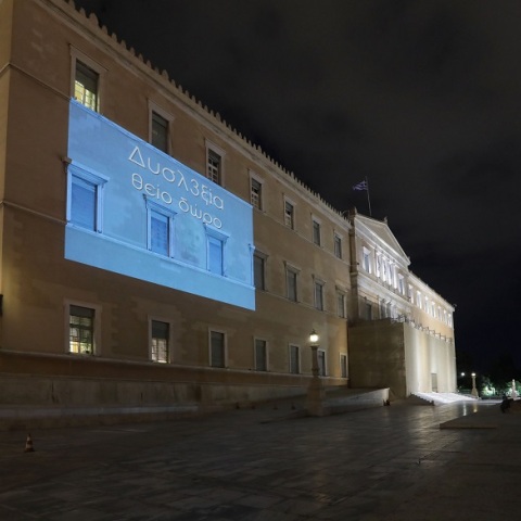 Η πρόσοψη του κτιρίου της Βουλής φωταγωγήθηκε με το σύνθημα «Δυσλ3ξία – Θείο Δώρο»