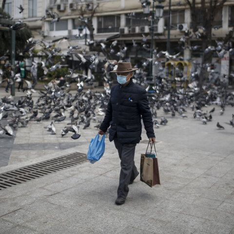 Ηλικιωμένος άνδρας με προστατευτική μάσκα για τον κορωνοϊό περπατά στο κέντρο της Αθήνας, κουβαλώντας τσάντες με ψώνια