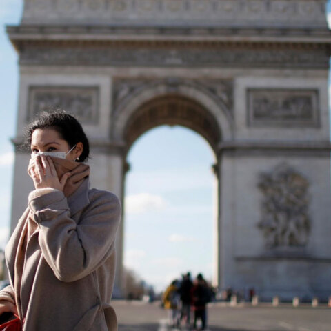 Γυναίκα με μάσκα για τον κορωνοϊό στο Παρίσι με φόντο την Αψίδα του Θριάμβου