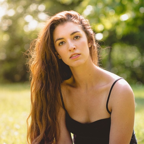 Γυναίκα με μακριά καστανά μαλλιά και μαύρη μπλούζα με τιράντα με φόντο δέντρα