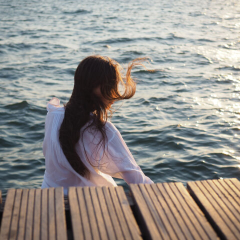 Κορίτσι καθισμένο δίπλα στη θάλασσα με γυρισμένη την πλάτη