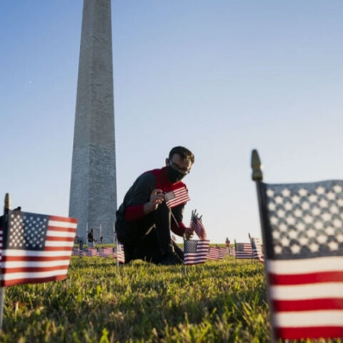 Άνδρας με προστατευτική μάσκα για τον κορωνοϊό τοποθετεί αμερικανικές σημαίες μπροστά από μνημείο στην πρωτεύουσα Ουάσινγκτον