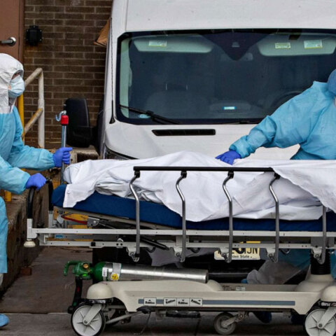 Τραυματιοφορείς στις ΗΠΑ με προστατευτικές στολές για τον κορωνοϊό σπρώχνουν φορείο με τη σορό ασθενούς Covid-19