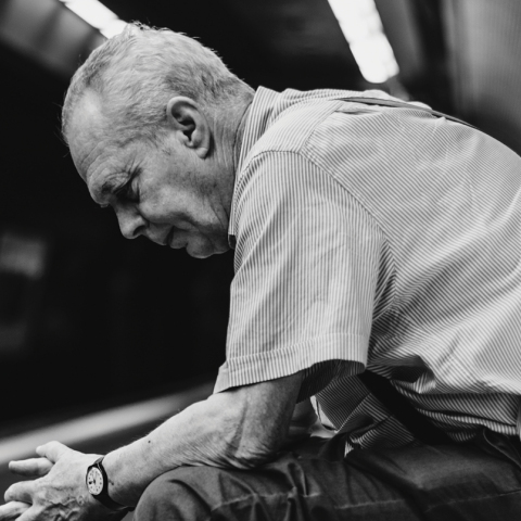 Ασπρόμαυρη φωτογραφία καθιστού ηλικιωμένου άνδρα σε σταθμό μετρό