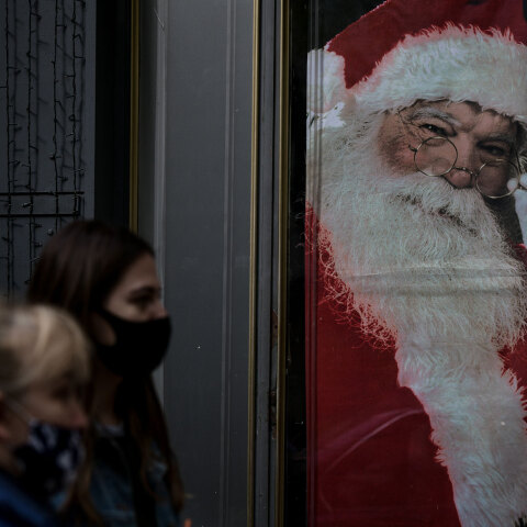 Πολίτες με μάσκα για τον κορωνοϊό στη Θεσσαλονίκη με φόντο εικόνα του Άγιου Βασίλη