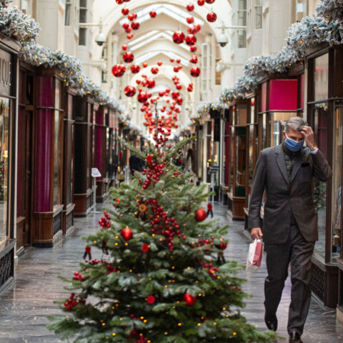 Άνδρας με προστατευτική μάσκα για τον κορωνοϊό περνά δίπλα από χριστουγεννιάτικο δέντρο στο Λονδίνο