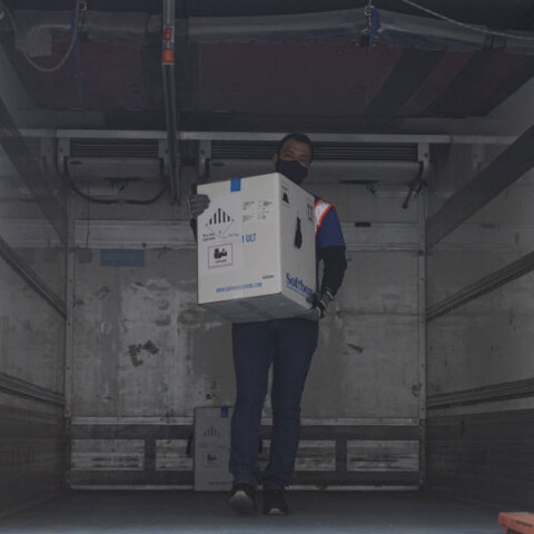 Κορωνοϊός - Κύπρος: Υπάλληλος με προστατευτική μάσκα για τον κορωνοϊό ξεφορτώνει τα πρώτα εμβόλια της Pfizer