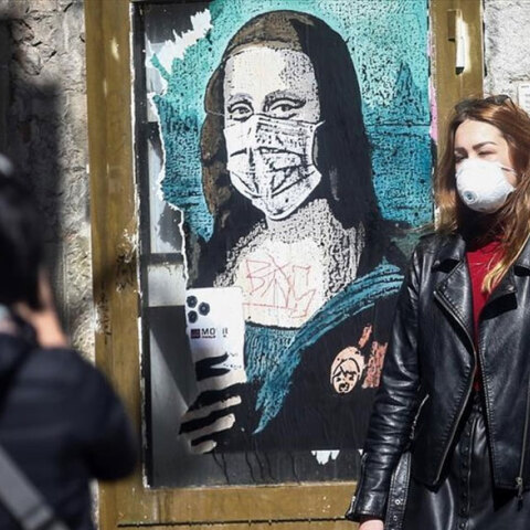 Γυναίκα με προστατευτική μάσκα για τον κορωνοϊό περνά μπροστά από γκράφιτι με την Τζοκόντα