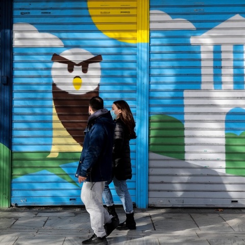 Πολίτες με μάσκα περπατούν μπροστά από κλειστά καταστήματα