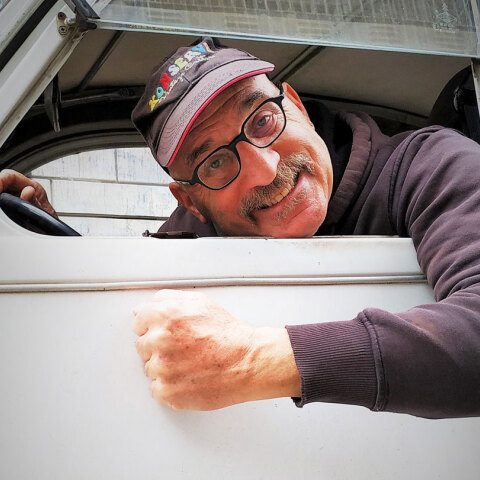 Άνδρας σε αυτοκίνητο σκυμένος στο τιμόνι κοιτάζοντας έξω από το παράθυρο το φωτογραφικό φακό