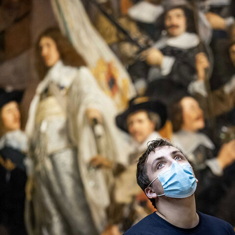Άμστερνταμ - Rijksmuseum: Νεαρός με μάσκα για τον κορωνοϊό με φόντο τον πίνακα «Νυχτερινή περίπολος» του Ολλανδού ζωγράφου Ρέμπραντ