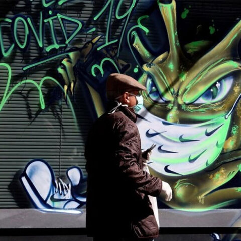 Άνδρας με μάσκα περνά μπροστά από γκράφιτι για τον κορωνοϊό