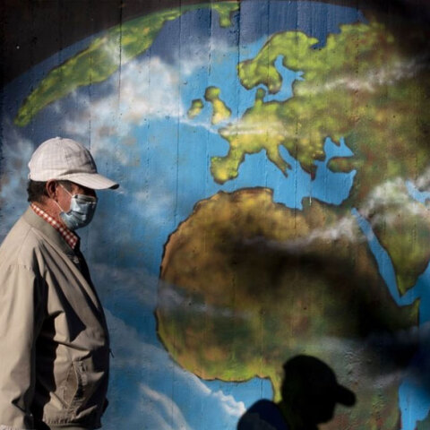 Άνδρας με προστατευτική μάσκα για τον κορωνοϊό περνά μπροστά από γκράφιτι με τον παγκόσμιο χάρτη της Γης