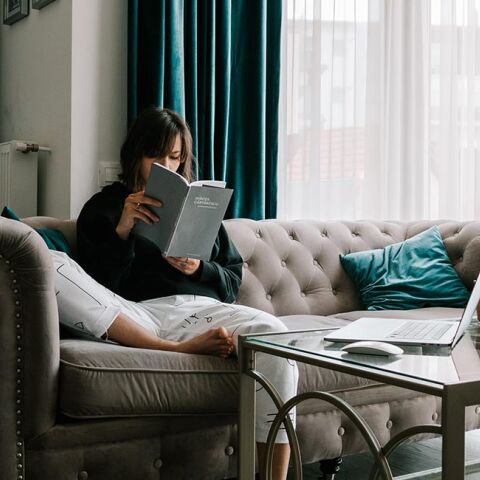Κοπέλα που κάθεται στον καναπέ και διαβάζει βιβλίο