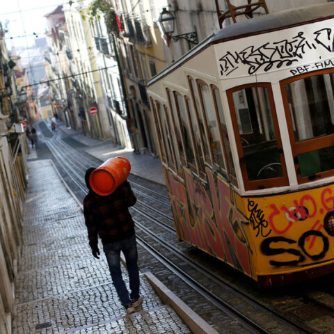 Πορτογαλία - Κορωνοϊός: Άνδρας κουβαλά φιάλη υγραερίου στην πλάτη δίπλα από συρμό του τραμ στη Λισαβόνα