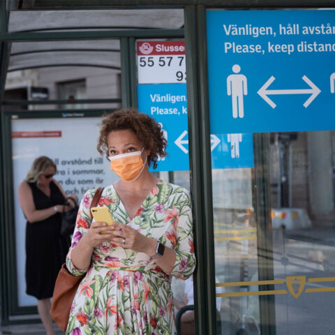 Κορωνοϊός: Κοπέλα με μάσκα και το κινητό στο χέρι περιμένει σε στάση λεωφορείου