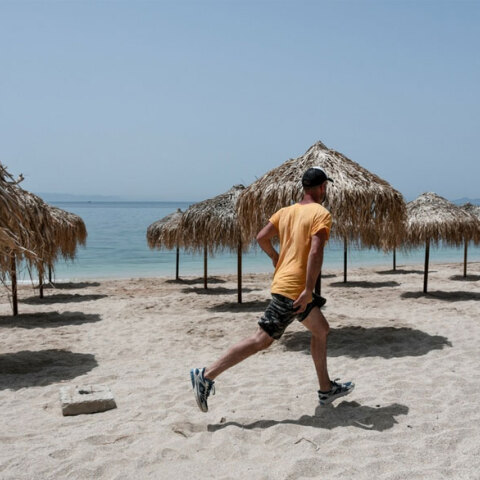 Άνδρας με μαγιό, αθλητικά παπούτσια και καπέλο τρέχει σε παραλία