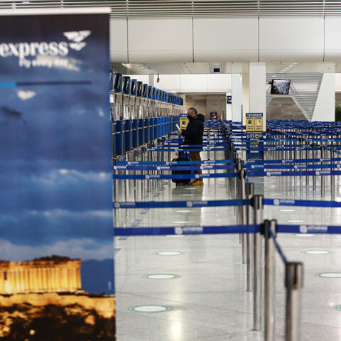 Διεθνές αεροδρόμιο «Ελευθέριος Βενιζέλος» στην εποχή του κορωνοϊού - Ταξιδιώτης με μάσκα ετοιμάζεται να δώσει τη βαλίτσα στο γκισέ και να τσεκάρει το εισιτήριό του
