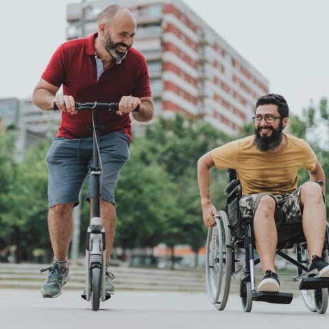 Άνδρας με πατίνι και άνδρας σε αναπηρικό αμαξίδιο
