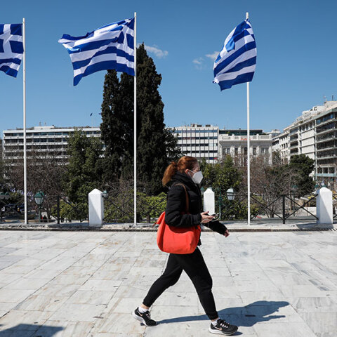 Γυναίκα με μάσκα για τον κορωνοϊό περνά από το Σύνταγμα όπου έχουν τοποθετηθεί ελληνικές σημαίες για τα 200 χρόνια από την Επανάσταση του 1821