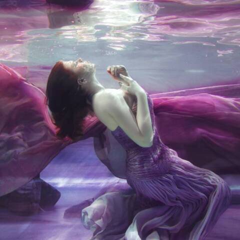 Γυναίκα με μοβ φόρεμα φωτογραφίζεται κάτω από το νερό