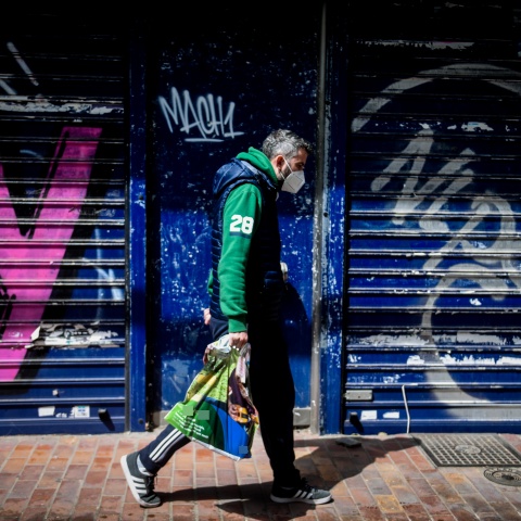 Πολίτης με μάσκα περπατά μπροστά από κλειστό κατάστημα