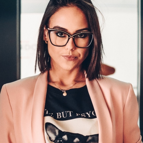 Γυναίκα στο ασανσέρ με καρέ μαλί, γυαλιά μυωπίας, μαύρη μπλούζα και ροζ σακάκι