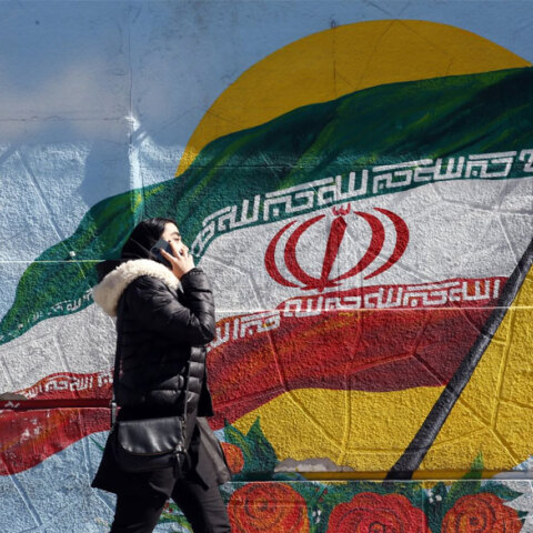 Ιρανή μιλά στο κινητό της τηλέφωνο περνώντας μπροστά από ένα γκράφιτι με τη σημαία του Ιράν στην πρωτεύουσα Τεχεράνη