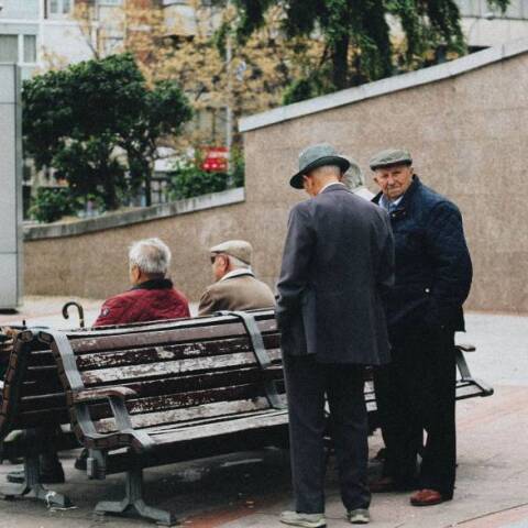 Ηλικιωμένοι άντρες στέκονται και συζητούν γύρω από ένα παγκάκι