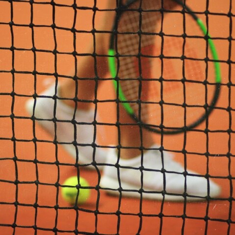 Παίκτρια του τένις κρατάει ρακέτα πίσω από το φιλέ©unsplash-John Fornander