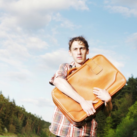 Άνδρας που περπατά στον δρόμο κρατώντας βαλίτσα στην αγκαλιά του