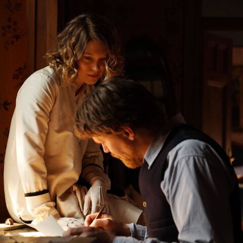 Γυναίκα που κάθεται πάνω σε γραφείο και κοιτά άνδρα που γράφει