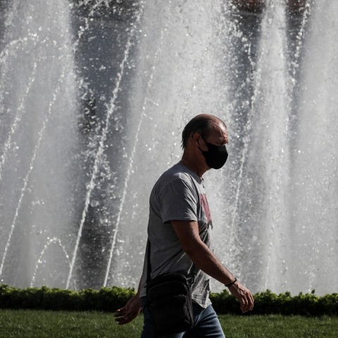 Πολίτης φορά μάσκα προστασίας κατά του κορωνοϊού και περπατά μπροστά από σιντριβάνι