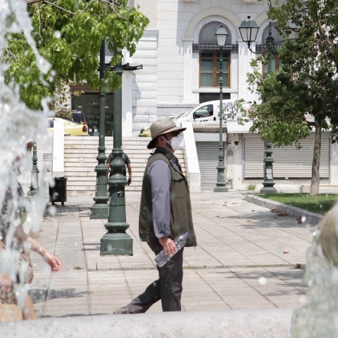 Πολίτης φορά τη μάσκα του και το καπέλο του περπατώντας στην πλατεία Συντάγματος